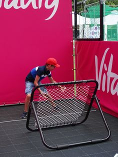 a young boy is playing tennis on an indoor court with pink and white banners behind him