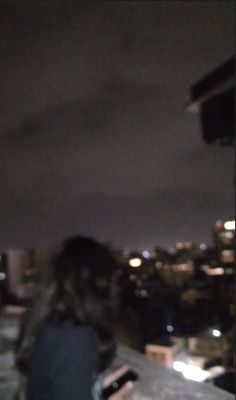 a woman looking at her cell phone while standing on the roof of a building with city lights in the background