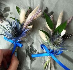 two flowers with blue ribbons tied around them on a sheet of white paper and being held by someone's hand