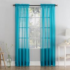 a living room with a window covered in blue sheer curtains and a wooden chair next to it