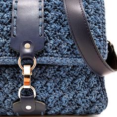 a blue crocheted bag with a leather handle and metal ring on the strap