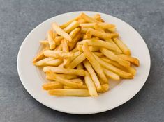 a white plate topped with french fries sitting on top of a gray countertop next to a knife and fork