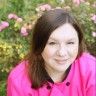 a woman in a pink shirt is posing for a photo with some flowers behind her