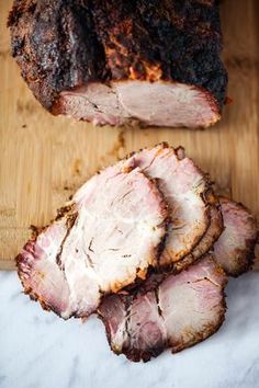 sliced pork on a cutting board with another meat in the back ground and one piece cut off