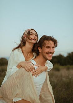 a man carrying a woman on his back in the middle of an open field at sunset