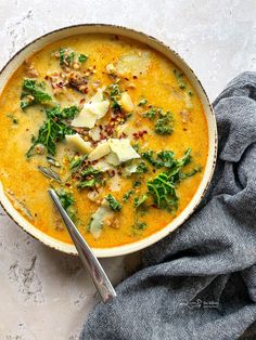 a bowl of soup with spinach, cheese and bread on the side next to a gray napkin