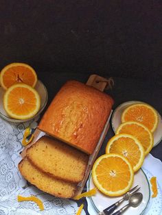 slices of orange pound cake on plates next to sliced oranges with forks and knife