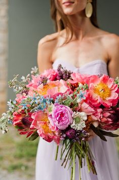 a woman in a white dress holding a large bouquet of pink, orange and yellow flowers