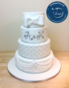 a three tiered white wedding cake with bow and monogrammings on it