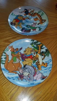 two winnie the pooh plates sitting on top of a wooden table