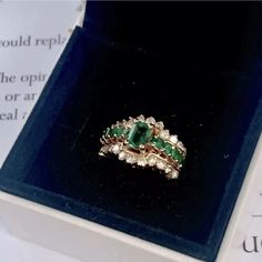 an emerald and diamond ring sits in a box on top of a piece of paper