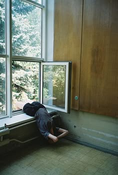 black and white photograph of a person sleeping on the window sill in an empty room