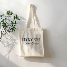 a lucky girl tote bag next to a plant