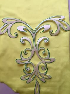 a yellow pillow with green and white designs on the front, sitting on a purple surface