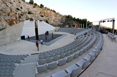 an empty outdoor seating area in front of a mountain with people standing on the stage