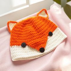 a crocheted fox hat laying on top of a pink blanket