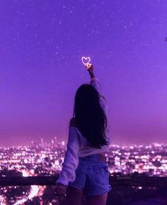 a woman holding up a heart shaped object in the air over a city at night