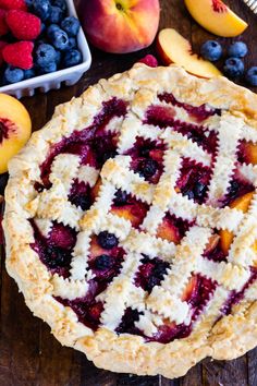 a pie sitting on top of a wooden table next to fresh berries and peaches