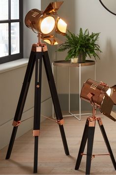 a tripod lamp with two spotlights on it and a potted plant in the corner