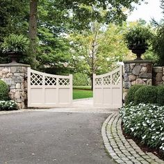 a driveway with stone walls and white flowers