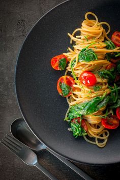 a black plate topped with pasta and veggies