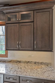 an empty kitchen with granite counter tops and wooden cabinetry, in front of a window