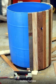 a large blue barrel sitting on top of a wooden floor next to plywood planks