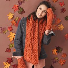 a woman wearing an orange knit scarf and mittens posing in front of fall leaves