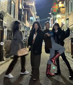 three women standing on the side of a street next to a brick building at night