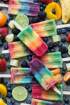 popsicles with fruit and limes are on a tray surrounded by other fruits, including strawberries, lemons, blueberries, raspberries, and oranges