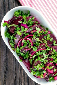 a bowl filled with beets and greens on top of a wooden table next to a striped cloth