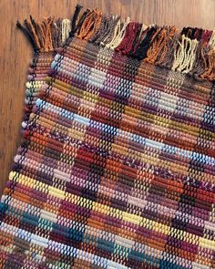 a multicolored rug with fringes on top of a wooden floor next to a remote control