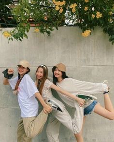 three young people posing for the camera in front of a cement wall with yellow flowers