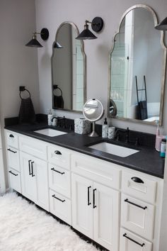 a bathroom with two sinks and three mirrors on the wall next to white rugs