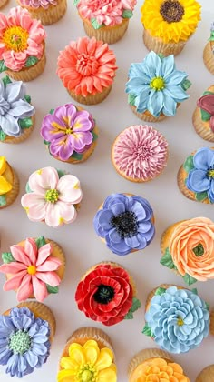 cupcakes decorated with colorful flowers are displayed on a white table top, ready to be eaten