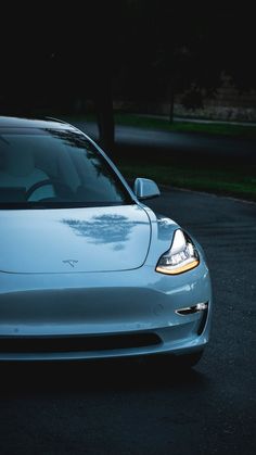 the front end of a silver car parked in a parking lot next to a tree