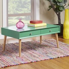 a green coffee table with two drawers and some books on it next to a yellow vase