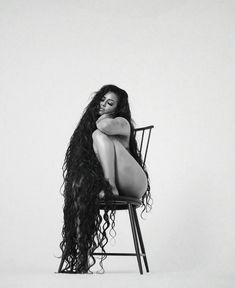 a woman sitting on top of a chair with her legs crossed and long hair blowing in the wind