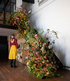 a woman in a yellow dress standing next to a bunch of flowers on the floor