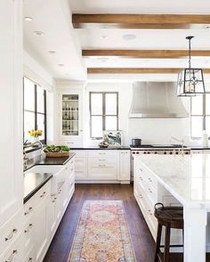 a large kitchen with white cabinets and wood beams on the ceiling, along with an area rug that matches the hardwood flooring