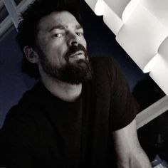 a man with a beard sitting in front of a light fixture and looking at the camera