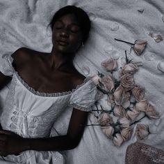 a woman laying on top of a bed covered in white sheets next to pink flowers