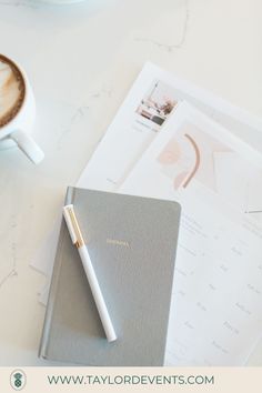 a cup of coffee next to a notebook and pen on top of a white table