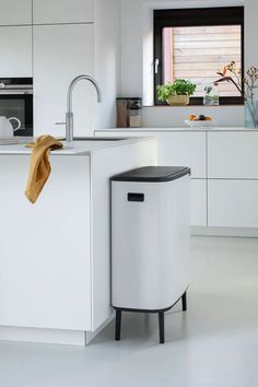 a black trash can sitting in the middle of a white kitchen with an open window