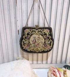 "This is a lovely 1920s petit point handbag, probably French or Austrian. Very popular during this era these wonderful bags were imported from Europe for the department stores. This bag has a pretty floral motif. The brass frame has nice intricate detail and black enameling. The brass clasp has a pretty floral design and is adorned with marcasites. Inside it is lined with nice ivory fabric and has one side pocket. It has a chain handle. The bag is in excellent vintage condition! The petit point is very clean, no stains or damage. The clasp and frame are straight and tight. The clasp is missing one marcasite, and the lining has some faint soiling at the edge from age and handling. Overall, a beautiful example from this era! The bag not including the handle measures 6 1/4\" W x 5\" L" Victorian Style Rectangular Evening Bag, Vintage Embellished Rectangular Bag, Vintage Bags With Gold-tone Hardware And Double Flap, Vintage Rectangular Flap Bag With Gold-tone Hardware, Vintage Tapestry Satchel With Top Handle, Vintage Evening Shoulder Bag With Gold-tone Hardware, Santa Margarita, Ivory Fabric, Department Stores