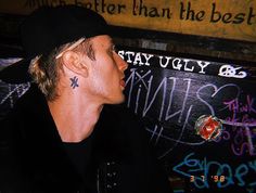 a man with a tattoo on his neck sitting in front of a sign that says stay ugly