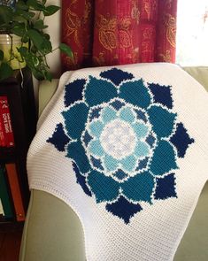 a blue and white crocheted blanket sitting on top of a couch next to a potted plant