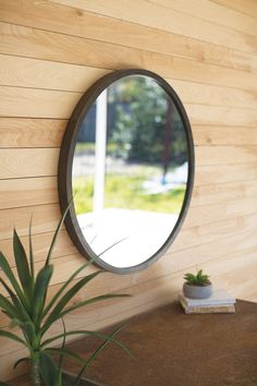 a round mirror hanging on the side of a wooden wall next to a potted plant