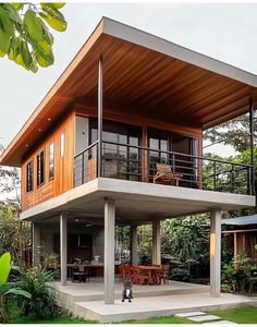 a modern house with an elevated deck and outdoor dining area on the second floor, surrounded by greenery