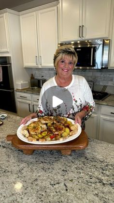 a woman holding a plate with food on it in a kitchen next to an oven